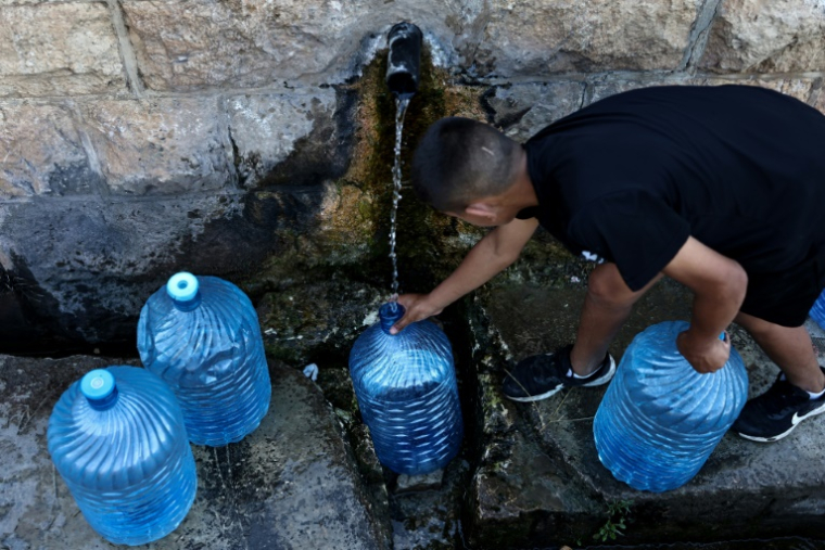 Un jeune Palestinien remplit des bouteilles d'eau provenant d'une source dans le village de Dura al-Qaraa, en Cisjordanie occupée, le 15 juillet 2025 ( AFP / Zain JAAFAR )
