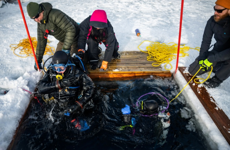 Un plongeur est extrait des eaux glacées lors d'un stage scientifique de plongée polaire, le 14 mars 2026 dans le lac de Kilpisjärvi, à l'extrême nord-ouest de la Finlande ( AFP / John MACDOUGALL )