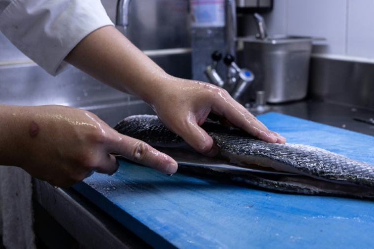 Un cuisinier prépare un bar dans la cuisine du restaurant L'Ambroisie du chef Bernard Pacaud, le 3 juillet 2025 à Paris ( AFP / JOEL SAGET )