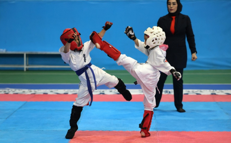 Deux fillettes participent à une compétition de karaté sous le regard d'une arbitre, à Téhéran le 6 novembre 2025 ( AFP / ATTA KENARE )