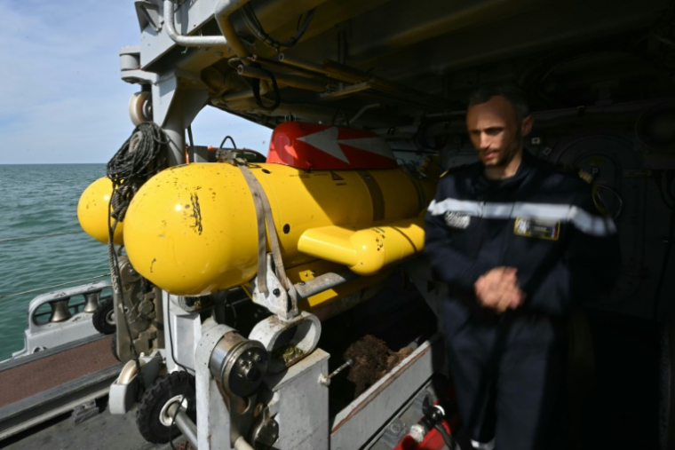 Le capitaine de corvette Jacquelin du Réau, commandant du chasseur de mines L'Aigle, à c^^oté d'un robot sous-marin jaune de déminag esur le pont du navire, au large de Dieppe, le 14 avril 2026 en Normandie ( AFP / Lou BENOIST )