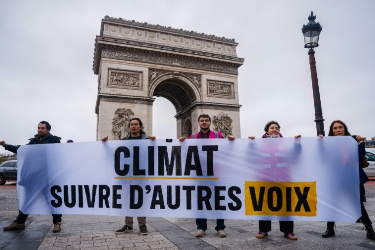 Des militants pour le climat brandissent une banderole devant l'Arc de triomphe à Paris le 12 décembre 2025 ( AFP / Dimitar DILKOFF )