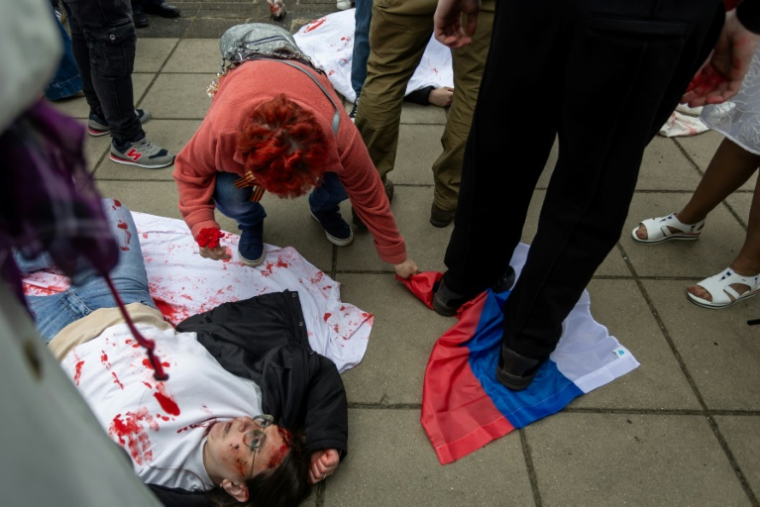 Une femme tente de récupérer un drapeau russe piétiné par un activiste pro-ukrainien lors d'une manifestation contre l'invasion russe de l'Ukraine, au mausolée des soldats soviétiques à Varsovie, le 9 mai 2025 en Pologne ( AFP / Wojtek RADWANSKI )