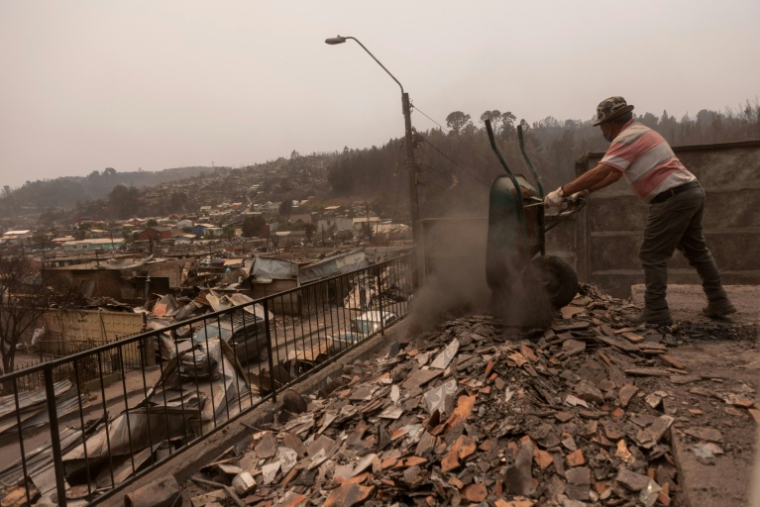Un homme déblaye les débris d'une maison incendiée dans le quartier Gabriela Mistral après un incendie de forêt à Lirquen, au Chili, le 19 janvier 2026 ( AFP / Raul BRAVO )