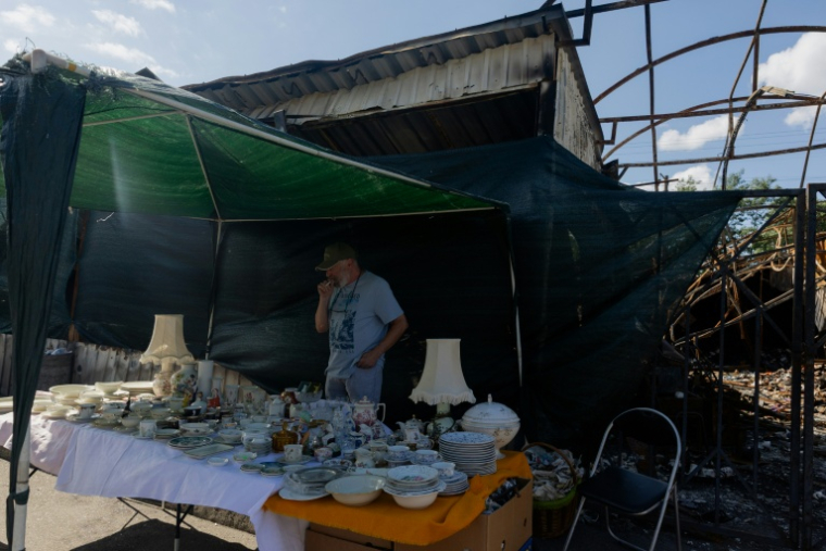 Vadym vend des objets sur son étal du marché aux puces de Potchaïna endommagé par une frappe russe, le 9 août 2026 à Kiev, en Ukraine ( AFP / Tetiana DZHAFAROVA )
