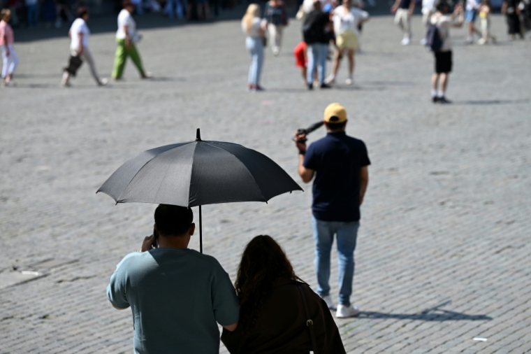 Des touristes visient Bruxelles à l'abri sous un parapluie pour se protéger du soleil lors d'une vague de chaleur le 27 mai 2026, en Belgique ( AFP / Nicolas TUCAT )
