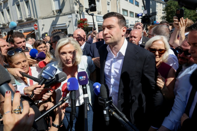 Marine Le Pen (c), cheffe du groupe parlementaire Rassemblement national (RN) et candidate à la présidentielle de 2027, et Jordan Bardella, président du RN, entourés par des journalistes à leur arrivée à La Flèche pour un rassemblement de campagne, le 8 juillet 2026 dans la Sarthe ( AFP / FRED TANNEAU )