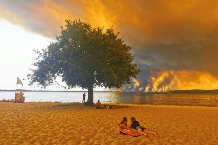 Des vacanciers sur une plage, à Lacanau, dans le sud-ouest de la France, le 24 juillet 2026, tandis que d'épais nuages de fumée s'élèvent dans le ciel au-dessus d'un incendie de forêt ( AFP / Maximilien LAMY )