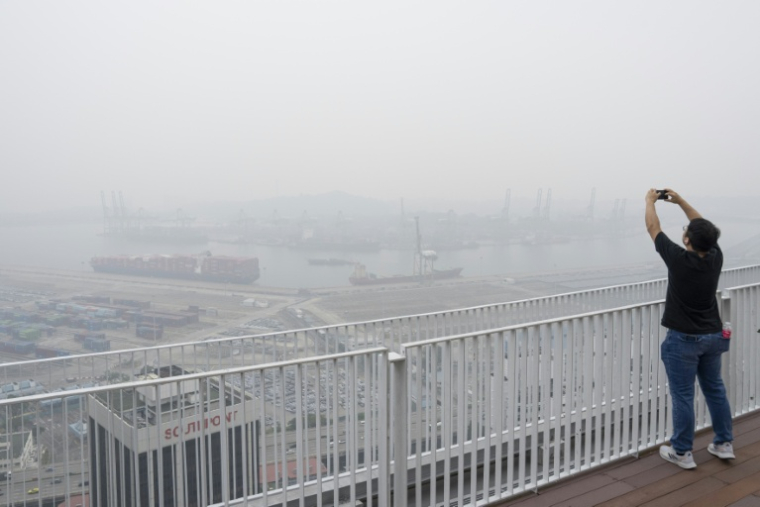 Un homme prend des photos depuis une plateforme d’observation à Singapour, enveloppé dans une brume causée par des incendies en Indonésie, le 16 octobre 2026 ( AFP / Yuichi YAMAZAKI )