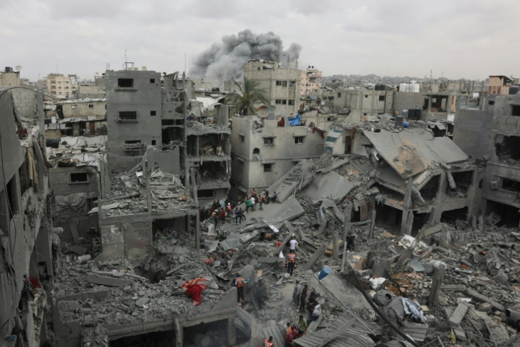 Des secouristes palestiniens inspectent site d'un bombardement israélien sur un immeuble résidentiel dans le quartier de Choujaïya à Gaza-ville, avec en arrière-plan un nuage de fumée, le 9 avril 2025 ( AFP / Omar AL-QATTAA )