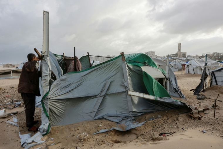 Un déplacé palestinien tente de réparer sa tente sous des vents violents sur une plage près de Gaza-ville, le 13 janvier 2026 ( AFP / Omar AL-QATTAA )