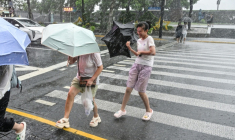 Des passants tentent de se protéger des fortes pluies du typhon Dolphin à Shanghai, le 10 août 2026 ( AFP / Hector RETAMAL )