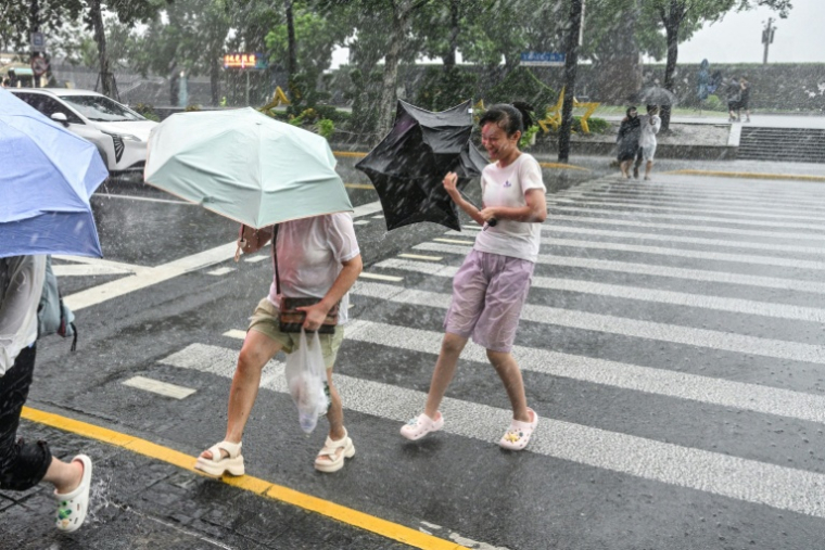Des passants tentent de se protéger des fortes pluies du typhon Dolphin à Shanghai, le 10 août 2026 ( AFP / Hector RETAMAL )