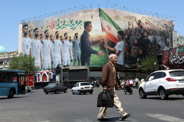 Un Iranien passe devant un panneau d'affichage géant mettant en scène l'équipe nationale iranienne de football qui a pris la direction de la Turquie pour y préparer le Mondial-2026, le 18 mai 2026 à Téhéran ( AFP / - )