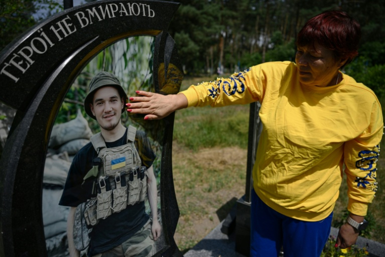 Nadia, 57 ans, mère du soldat ukrainien tué Andriï Doubnytsky, caresse son portrait sur sa tombe dans un cimetière du village de Stepantsi, dans la région de Tcherkassy, le 7 juillet 2026. ( AFP / Genya SAVILOV )