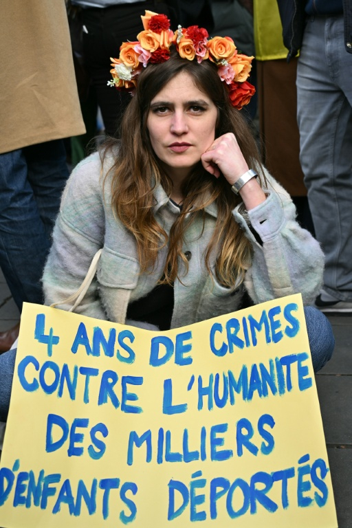 Une femme est assise derrière une pancarte où l'on peut lire « 4 ans de crimes contre l'humanité, des milliers d'enfants déportés » lors d'une marche pour l'Ukraine à Paris, à l'approche du quatrième anniversaire de l'invasion russe, le 21 février 2026 ( AFP / Bertrand GUAY )