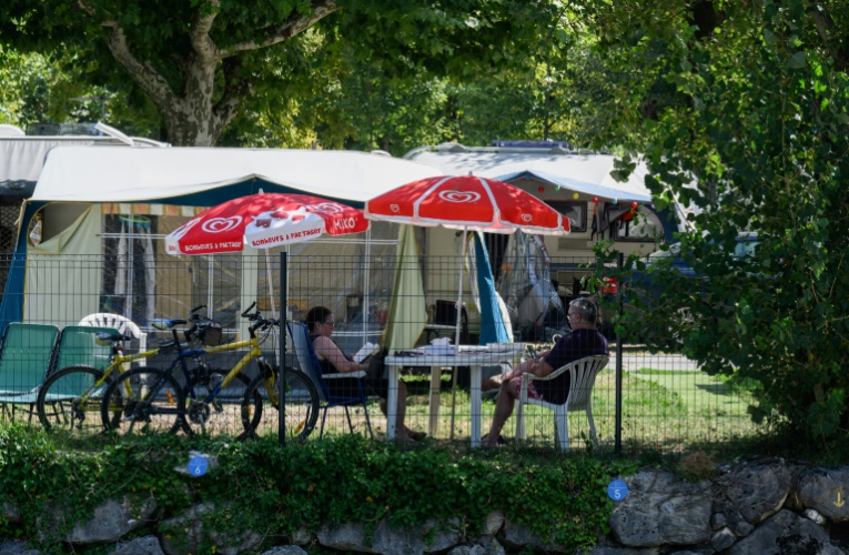 Des vacanciers assis à l'ombre dans un camping au Bourget-du-Lac, le 8 août 2025 en Savoie ( AFP / JEAN-PHILIPPE KSIAZEK )