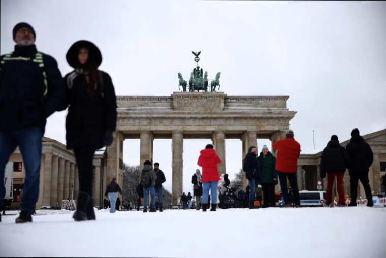 Des passants devant la porte de Brandebourg, enneigée, à Berlin