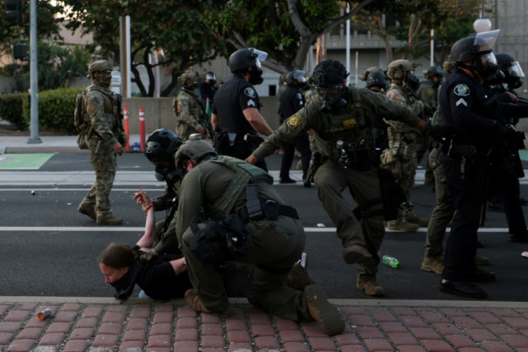 Des membres de la police des frontières plaquent au sol une manifestante à Santa Ana, en Californie, près du bureau des Services de l'Immigration, le 9 juin 2025, lors de protestations contre la politique migratoire de Donald Trump ( AFP / Patrick T. Fallon )