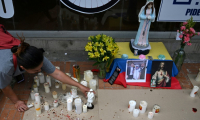 Une femme allume des bougies devant la clinique Santa Fe, où le sénateur Miguel Uribe est hospitalisé après avoir été blessé par balle lors d'un meeting politique, le 10 juin 2025 à Bogota, en Colombie ( AFP / Raul ARBOLEDA )