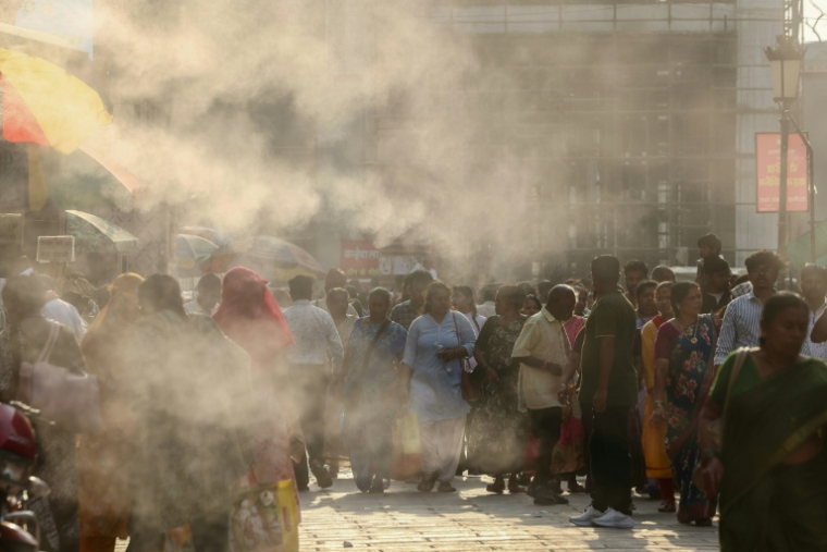 Des passants dans une rue rafraichie par des brumisateurs à Varanasi, en Inde, en pleine vague de chaleur le 15 mai 2026 ( AFP / Niharika KULKARNI )