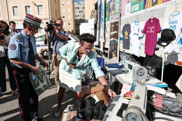 Corinne Simon (au centre), déléguée du préfet de police des Bouches-du-Rhône, examine des produits contrefaits lors de leur présentation avant leur destruction à Marseille, dans le sud-est de la France, le 18 juin 2026 ( AFP / Thibaud MORITZ )