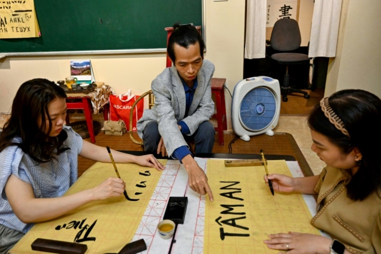 Le calligraphe Nguyen Thanh Tung (c) enseigne la calligraphie à des étudiants, chez lui à Hanoï, le 15 mai 2025 au Vietnam ( AFP / Nhac NGUYEN )