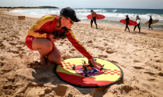 La secouriste Eliza Heys vérifie un drone après son atterrissage sur une plage à Sydney, le 1er octobre 2025 ( AFP / DAVID GRAY )