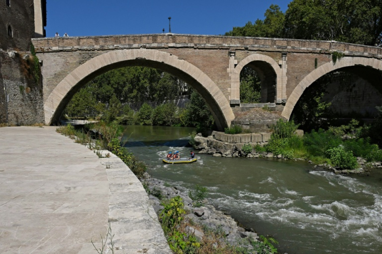 Des personnes naviguent en canot pneumatique sur le Tibre, passant devant l'île Tibérine, sur un tronçon du fleuve situé entièrement dans la zone urbaine du centre de Rome, le 14 août 2026 ( AFP / Andreas SOLARO )