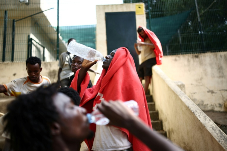 Des migrants boivent de l'eau devant le centre d'accueil de courte durée pour migrants de Ceuta, enclave espagnole en Afrique du Nord, le 1er août 2026 ( AFP / Henry Nicholls )