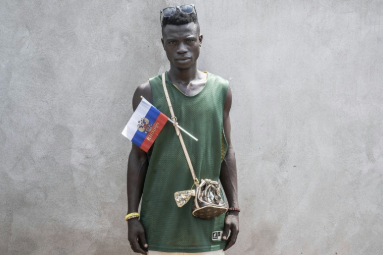 Un manifestant arbore un drapeau russe orné de l'emblème de la Russie accroché à la bandoulière de son sac lors d'une marche de soutien à la présence russe et chinoise en République centrafricaine, le 22 mars 2023 à Bangui ( AFP / Barbara DEBOUT )