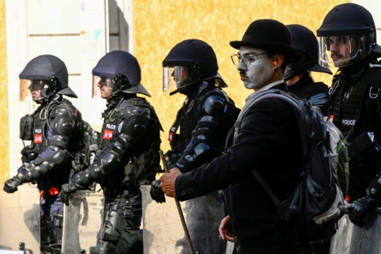 Un homme grimé en Charlie Chaplin à côté de policiers suisses en tenue antiémeute lors d'un rassemblement de la coalition "Non au G7", le 14 juin 2026 à Genève, en Suisse, à la veille du début du sommet du G7 à Evian, en France ( AFP / Gabriel Monnet )