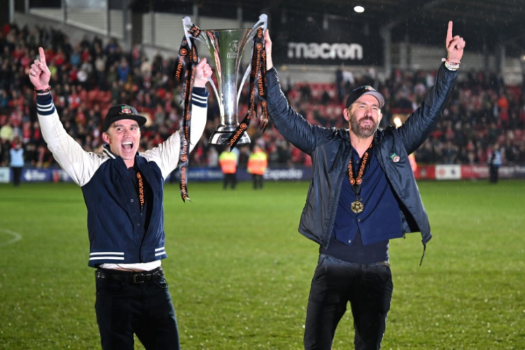 Les acteurs Rob McElhenney (g) et Ryan Reynolds, propiétaires du cludb de Wrexham, avec le trophée de National League (5e div.), le 22 avril 2022 ( AFP / Oli SCARFF )