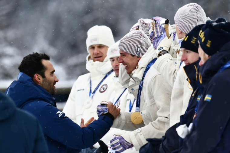 L'ancien biathlète Martin Fourcade félicite Quentin Fillon Maillet sur le podium du relais des JO-2026 le 17 février 2026 à Anterselva ( AFP / Marco BERTORELLO )