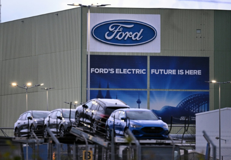 Des voitures du constructeur automobile américain Ford sont alignées sur un camion transporteur devant le logo de l'entreprise à l'usine Ford de Cologne, dans l'ouest de l'Allemagne, le 25 novembre 2024 ( AFP / Ina FASSBENDER )