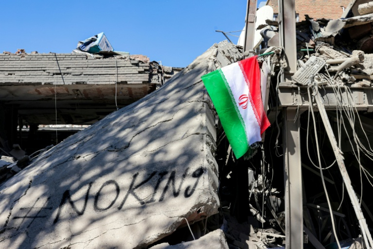 Un drapeau iranien dans les décombres d’un bâtiment effondré, à côté d’un graffiti portant l’inscription « #NoKing », après des frappes contre l’Université de technologie Sharif à Téhéran, le 7 avril 2026 ( AFP / ATTA KENARE )