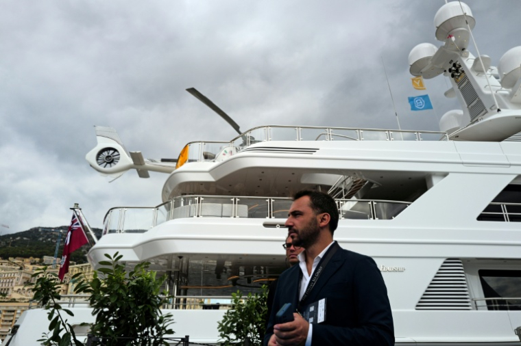 Un homme passe devant un superyacht amarré au port Hercule, avec un hélicoptère sur le pont, lors du Monaco Yacht Show, le 23 septembre 2026 ( AFP / Valery HACHE )