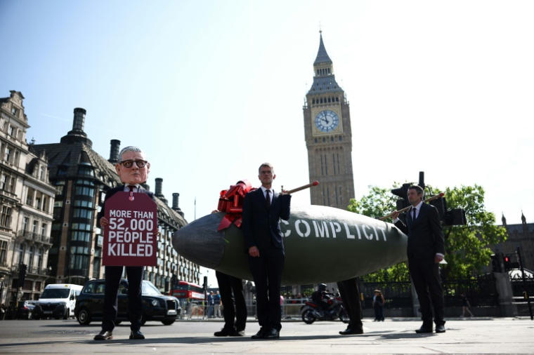 Un manifestant déguisé en Premier ministre britannique Keir Starmer pose devant une réplique d'une bombe et porte une pancarte indiquant "plus de 52.000 personnes tuées", près du palais de Westminster à Londres, le 12 mai 2025 ( AFP / HENRY NICHOLLS )