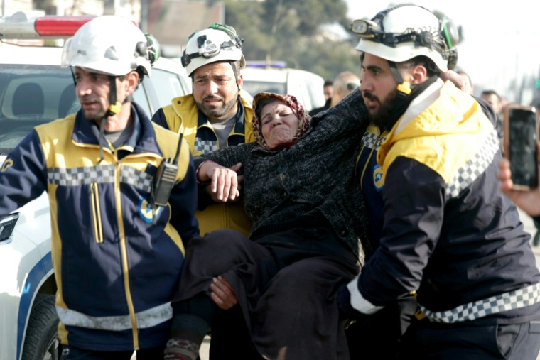Des membres de la Défense civile syrienne aident une femme déplacée ayant fui les quartiers kurdes d'Alep, encerclés par l'armée, le 8 janvier 2026 ( AFP / OMAR HAJ KADOUR )