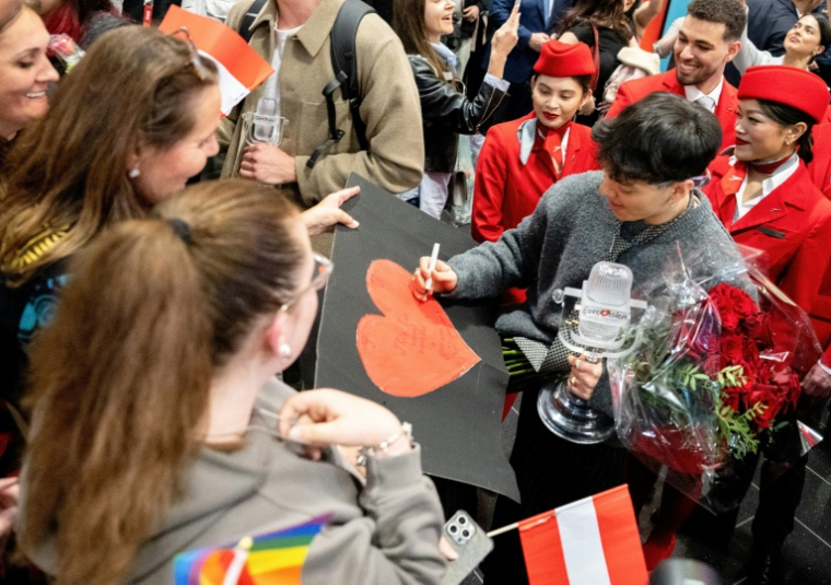 Le chanteur autrichien JJ, vainqueur de l'Eurovision, signe des autographes pour ses fans, lors de son arrivée à l'aéroport de Vienne, le 18 mai 2025 ( AFP / JOE KLAMAR )