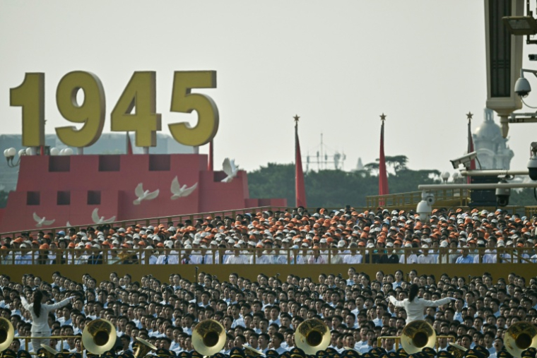 Des personnes chantent derrière une fanfare militaire avant un défilé militaire marquant le 80e anniversaire de la victoire sur le Japon et la fin de la Seconde Guerre mondiale, sur la place Tiananmen de Pékin le 3 septembre 2025 ( AFP / Pedro Pardo )