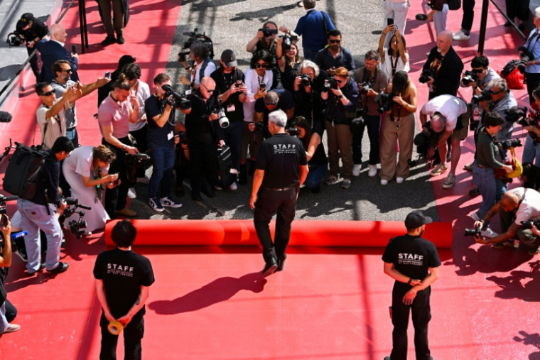 Un employé déroule le tapis rouge devant le Palais des Festivals à Cannes le 12 mai 2026 ( AFP / Antonin THUILLIER )