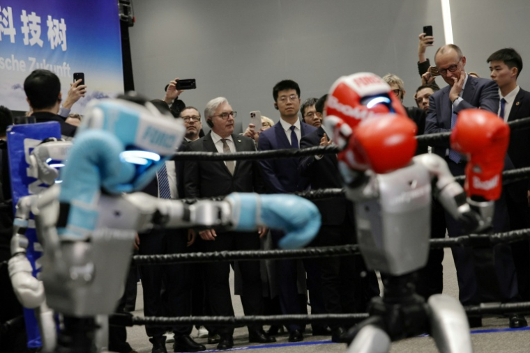 Le chancelier allemand Friedrich Merz (2e d) observe un combat de boxe entre deux robots humanoïdes dans une salle d'exposition des produits Unitree Robotics à Hangzhou, dans l'est de la Chine, le 26 février 2026  ( POOL / ANDRES MARTINEZ CASARES )