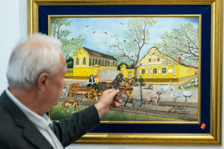 Le galeriste Pavel Babka montre des détails sur un tableau d'art naïf à Kovačica, dans le nord de la Serbie, le 16 octobre 2025 ( AFP / Andrej ISAKOVIC )