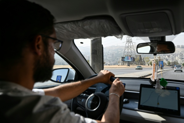 Ahmad al-Lahham, chauffeur pour l'une des principales applications de taxis "Yalla Go", au volant son véhicule hybride rechargeable à Damas, le 25 octobre 2026 en Syrie ( AFP / LOUAI BESHARA )
