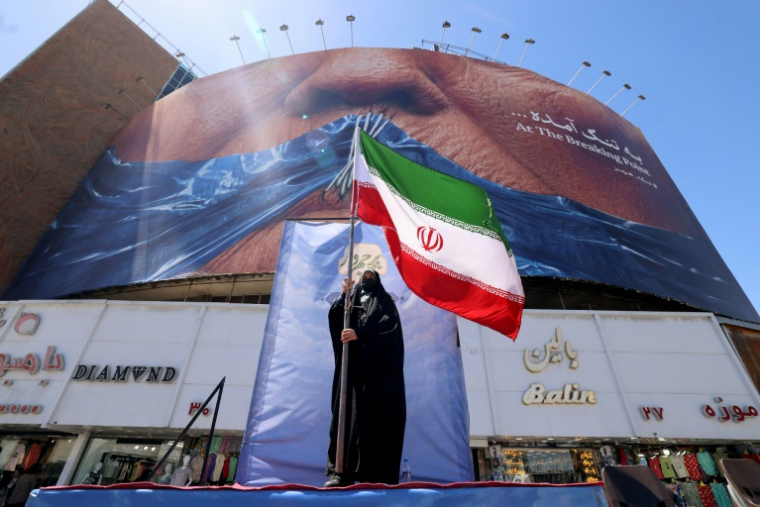 Une Iranienne brandit le drapeau de son pays, devant une panneau représentant le président américain Donald Trump, à Téhéran le 10 mai 2026 ( AFP / ATTA KENARE )