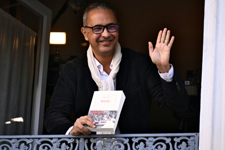 L'écrivain algérien Kamel Daoud, lauréat du Prix Goncourt pour son roman "Houris", salue depuis la fenêtre du restaurant Drouant à Paris, le 4 novembre 2024 ( AFP / JULIEN DE ROSA )