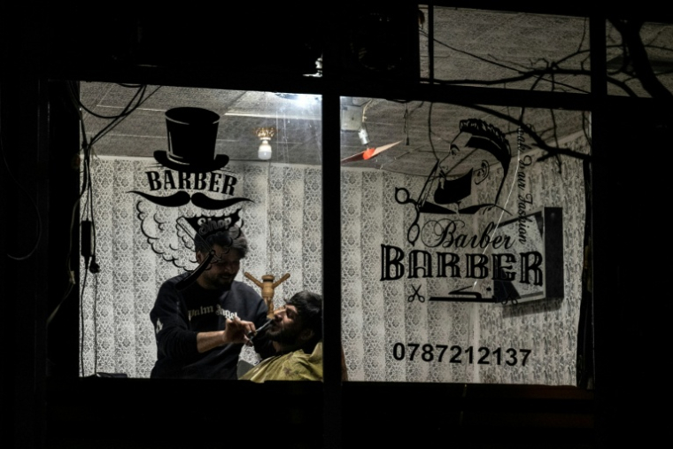 Un barbier taille la barbe d'un client dans un salon à Kaboul le 11 février 2026 ( AFP / Wakil KOHSAR )