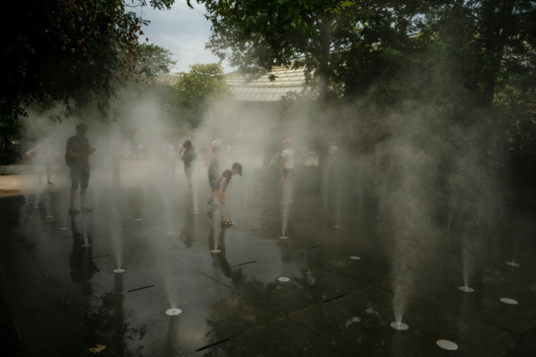 Des enfants se rafraîchissent dans une fontaine à brume dans le centre de Paris le 13 août 2025, en pleine canicule ( AFP / Dimitar DILKOFF )