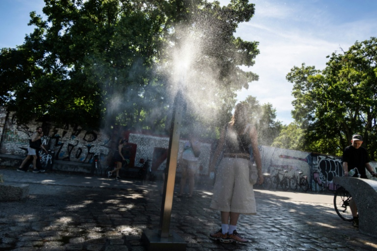 Une femme se rafraîchit à une fontaine brumisatrice à Berlin, le 22 juin 2026 lors d'un épisode de canicule en Europe ( AFP / John MACDOUGALL )